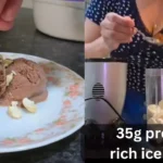 Creamy 35g protein-rich chocolate ice cream in a bowl with a scoop, topped with dark chocolate chips and almonds, next to a protein powder container and a dumbbell.